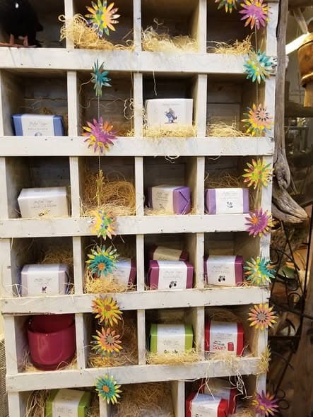 A wooden cubby shelf of wrapped artisan soaps trimmed with bright paper flowers