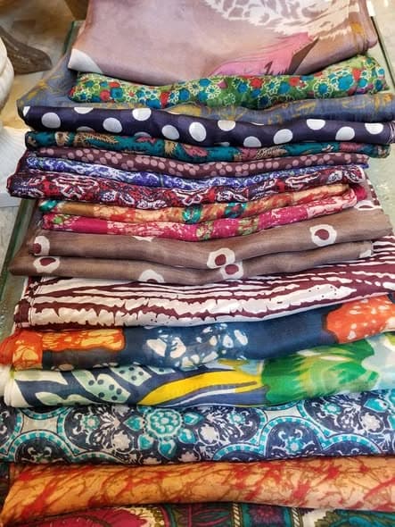 A tall stack of folded scarves in rich plum, teal, marigold, and indigo prints